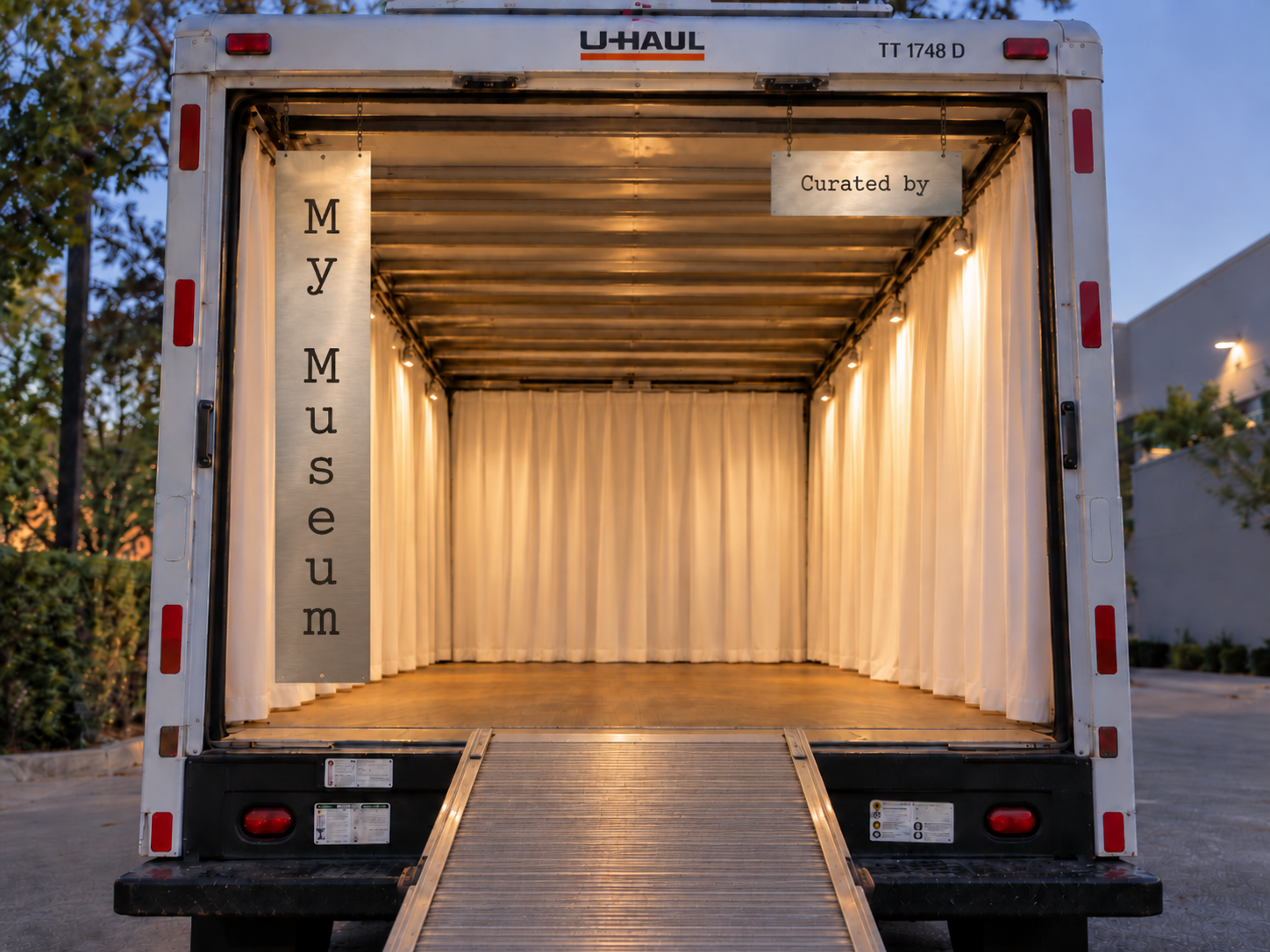 The interior of the My Museum UHAUL truck — open ramp, gallery lighting, white curtains, and the My Museum sign hanging inside